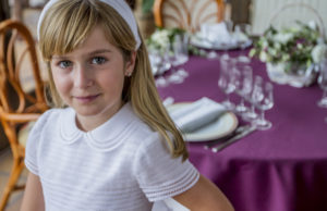 Niña con vestido de comunión sonriente con un banquete de fondo